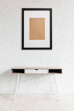 Modern masa ayakta beyaz tuğla duvara asılı siyah çerçeve yakınındaki halıda 