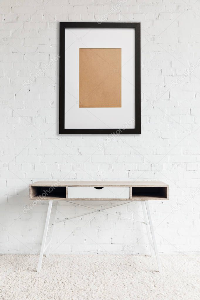 modern table standing on carpet near black frame hanging on white brick wall 