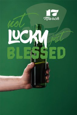 cropped view of man holding beer bottle near not lucky just blessed lettering on green background clipart