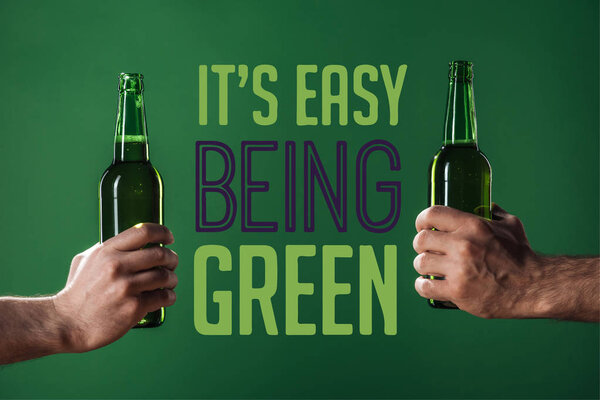 обрезанный вид мужчин, держащих пивные бутылки рядом с его легко зеленые буквы на зеленом фоне
