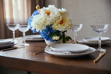 Beyaz tabaklar, kristal bardak ve evde ahşap masaya çiçek