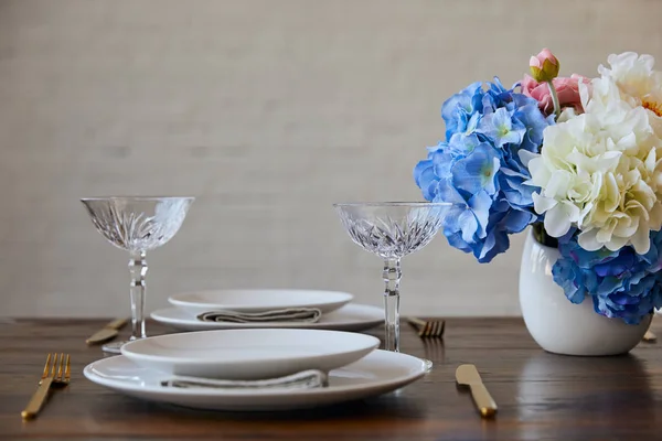 白プレート ナイフし フォーク クリスタル ガラス れんが造りの壁を自宅近くの木製のテーブルの上に花瓶の花束 — ストック写真