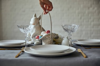 sepet beyaz tabaklar, kristal bardak ve dekoratif bunnie yakınındaki boyalı yumurta ile evde masaya koyarak kadın kırpılmış görünümünü
