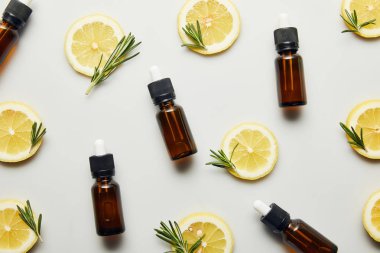 Düz ile şişe uçucu yağ, limon dilimleri ve biberiye gri arka plan üzerinde göklere