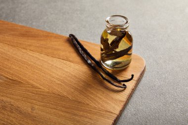 Vanilla pods and bottle with essential oil on wooden surface clipart