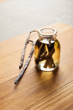 Glass bottle of essential oil with vanilla pods on wooden cutting board clipart
