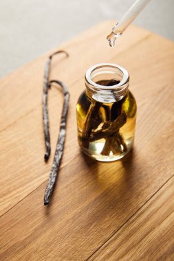 Glass bottle of essential oil with vanilla pods on wooden cutting board clipart