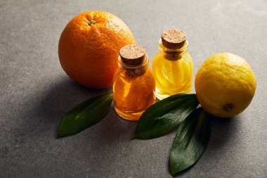 Bottles of essential oil with orange and lemon on dark surface clipart