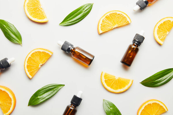 Flat lay with essential oil bottles, orange slices and green leaves on white background