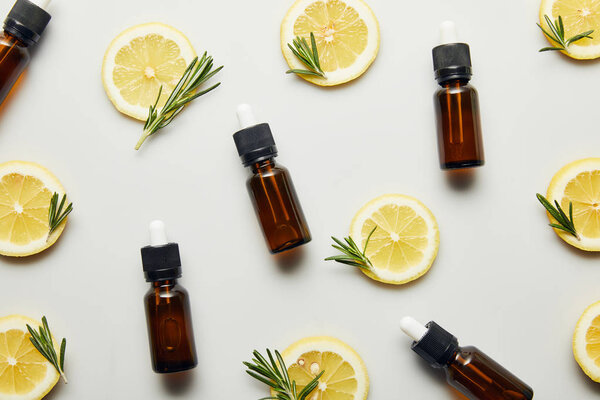 Flat lay with bottles of essential oil, lemon slices and rosemary on grey background