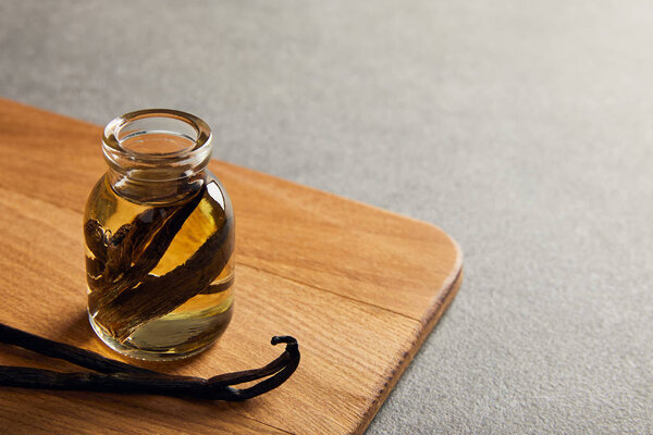 Vanilla pods and essential oil on wooden cutting board on dark surface