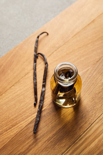 Top view of essential oil with vanilla pods on wooden surface