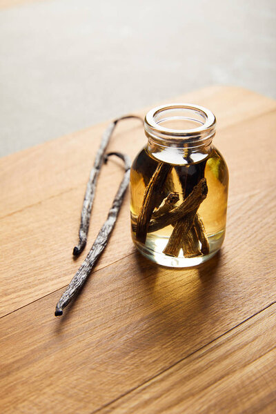 Стеклянная бутылка эфирного масла с ванильными стручками на деревянной доске
