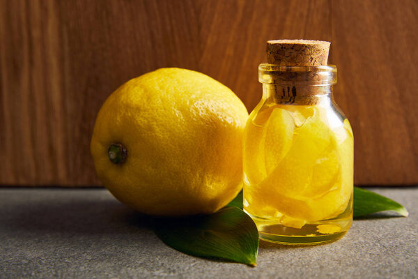 Whole lemon with bottle of essential oil on dark surface