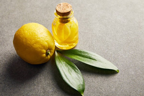 Whole lemon and glass bottle with essential oil on dark surface