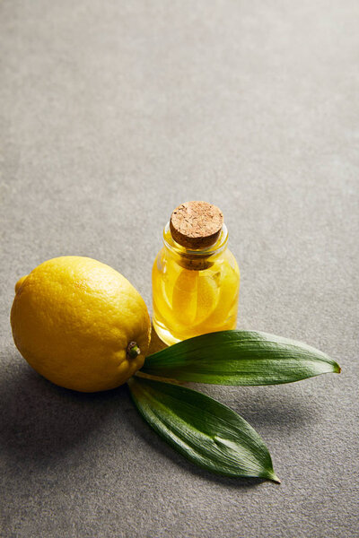 Whole lemon with green leaves and glass bottle with essential oil on dark surface