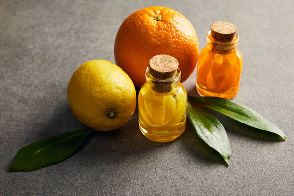 Bottles of essential oil with lemon and orange on dark surface