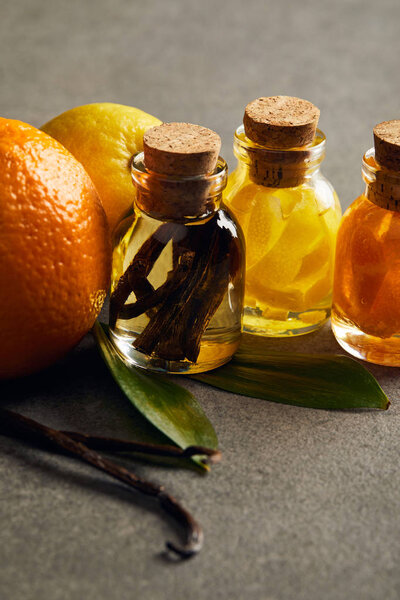 Bottles of essential oil with lemon, orange and vanilla on dark surface