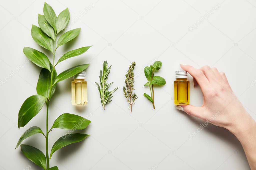 Partial view of woman holding bottle with essential oil on white background
