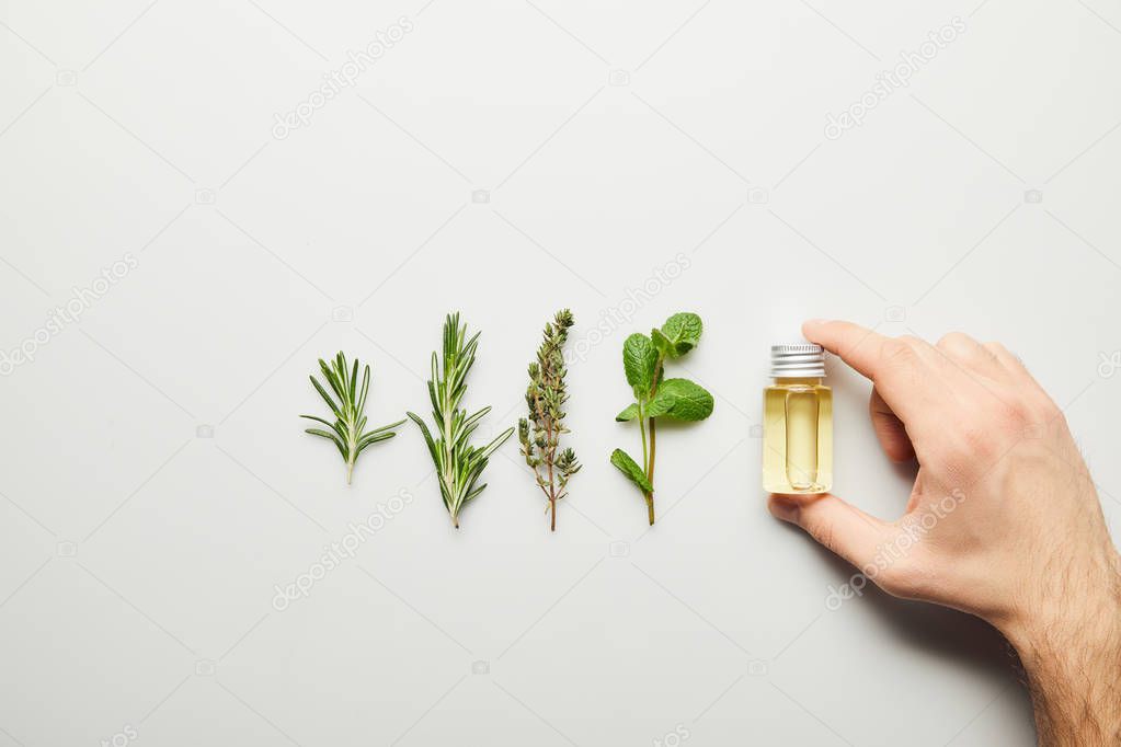 Partial view of man holding bottle of essential oil on white background