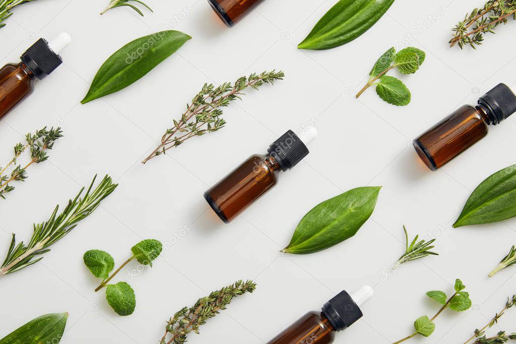 Flat lay with bottles on essential oil and green herbs on grey background