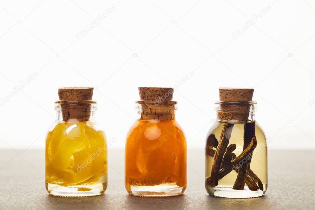 Bottles of essential oil with cut lemon, orange and vanilla on white background