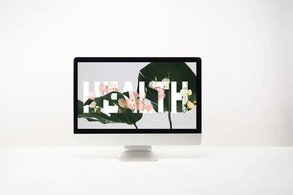 computer with health lettering and tropical green leaves on monitor on desk on white background