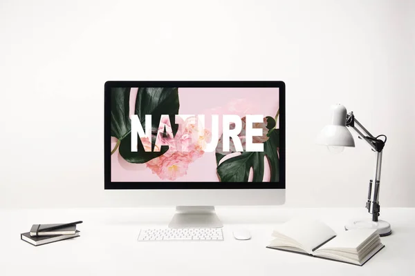 computer with nature lettering and green tropical leaves and roses on monitor on desk on white background