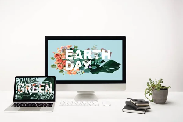 computer with earth day lettering on monitor and laptop with green lettering on screen on desk on white background