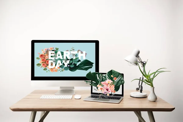モニターの地球日図でコンピューターとラップトップ モンステラの葉し 花を木製のテーブル上の画面の図 — ストック写真