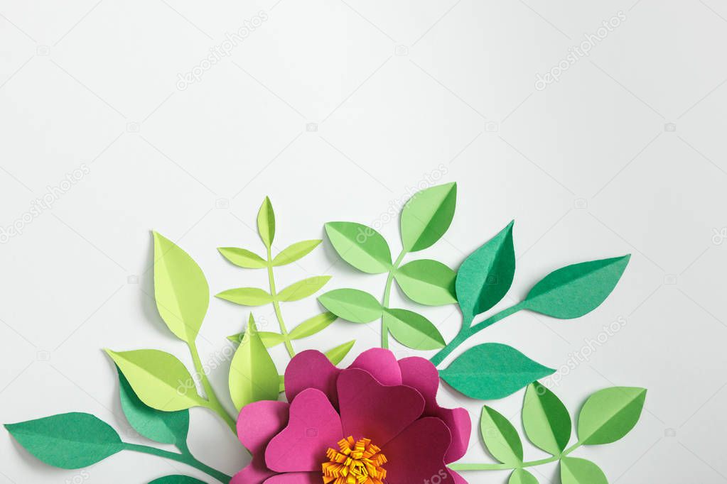 top view of pink paper flower and green plants on grey background