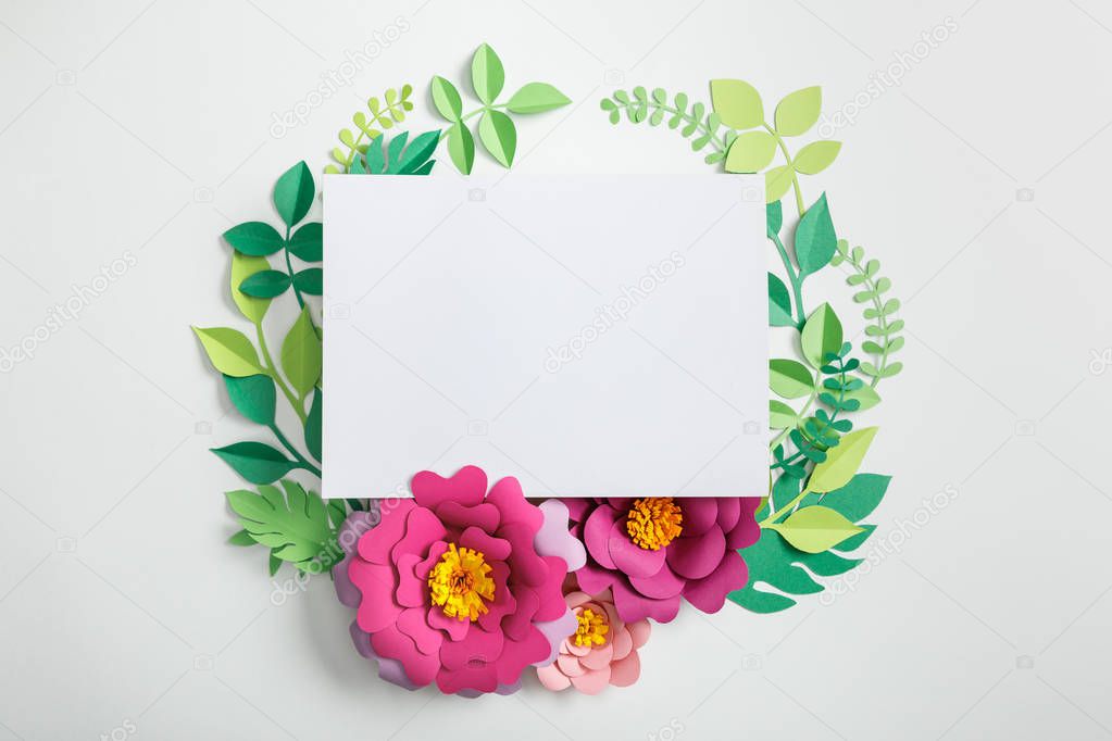 top view of white blank card near pink paper flowers with green leaves on grey background
