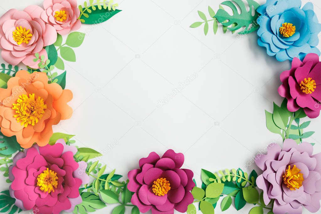 top view of colorful paper flowers and green plants with leaves on grey background