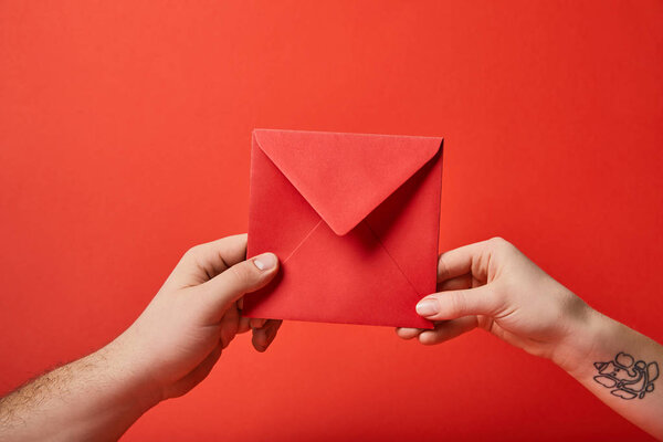 partial view of woman with tattoo and man holding red envelope on red background 
