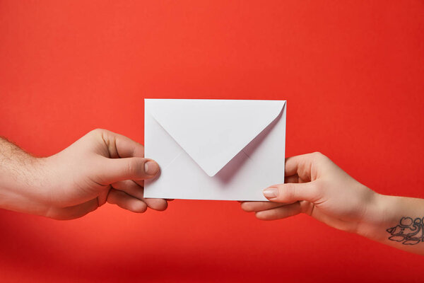 cropped view of woman with tattoo and man holding white envelope on red background 