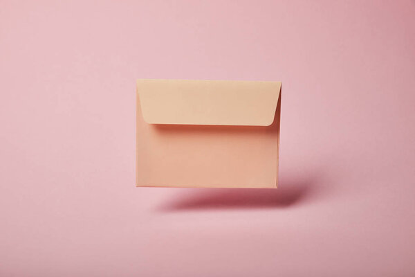 beige and empty envelope on pink background with copy space