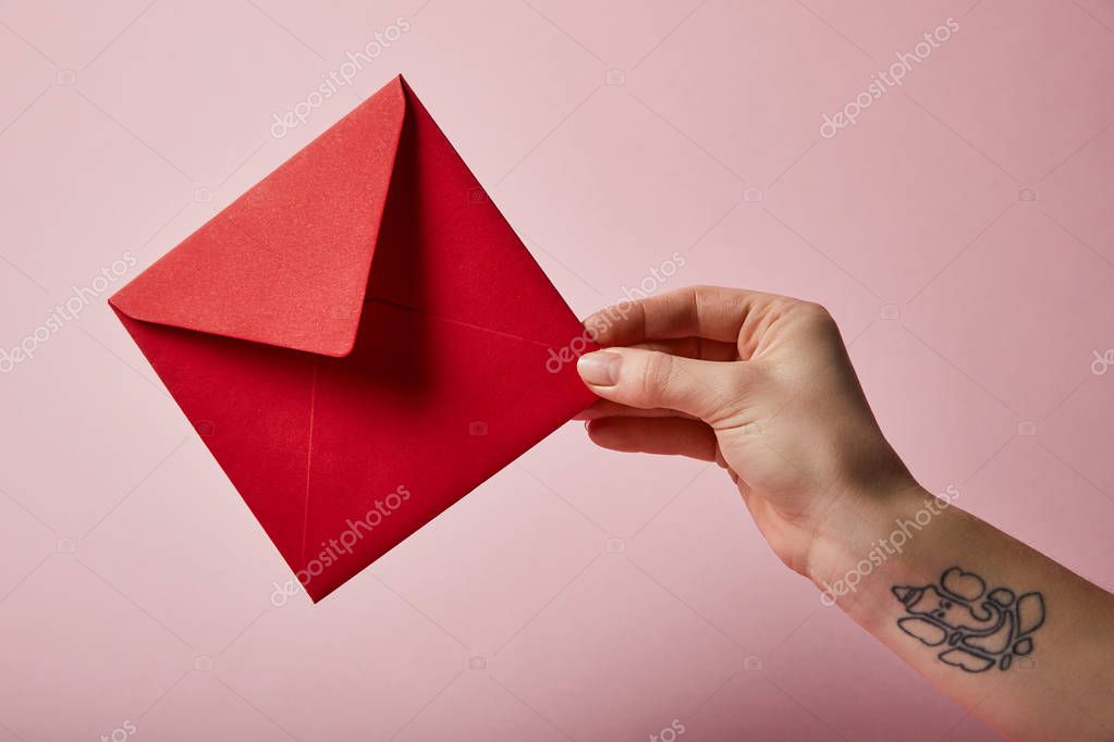 Partial view of woman with tattoo holding red envelope on pink background