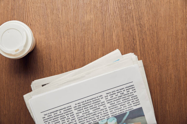 top view of newspaper near paper cup on wooden surface 