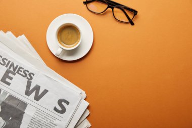 top view of glasses near business newspaper and cup of coffee on orange  clipart