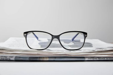 selective focus of glasses near newspaper on white  clipart