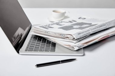 selective focus of laptop with blank screen near business newspapers, pen and cup  clipart