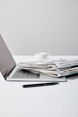 Gazeteler, kalem ve gri bardakta yakınındaki boş ekran ile dizüstü seçici odak 