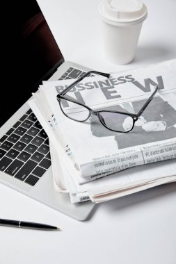 laptop with blank screen near business newspapers,glasses, pen and paper cup on white  clipart