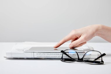 cropped view of woman using digital tablet near newspaper and glasses on white 