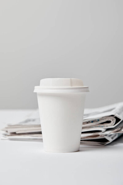 selective focus of paper cup near newspapers on grey 