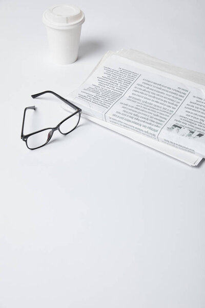 glasses near paper cup and newspapers on white 