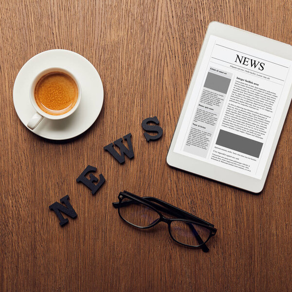 top view of digital tablet near news lettering, glasses and cup of coffee