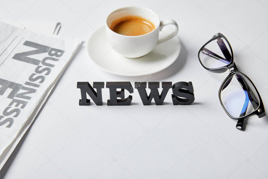 news lettering near cup of coffee, glasses and business newspaper on white 