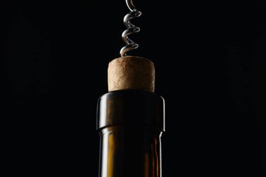 Close up view of glass wine bottle with wooden cork and corkscrew isolated on black clipart