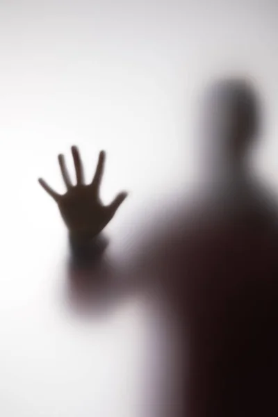 Blurry silhouette of person touching glass with hand